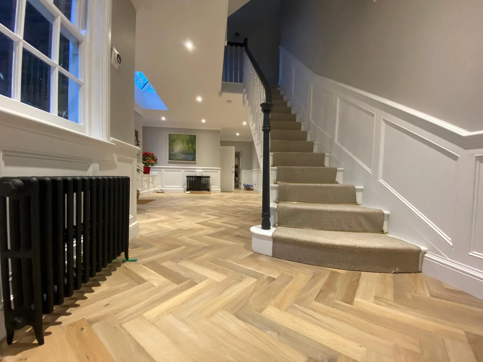 Carpet stair runner fitted on a curved staircase above a light herringbone oak hallway floor | Northfold Flooring
