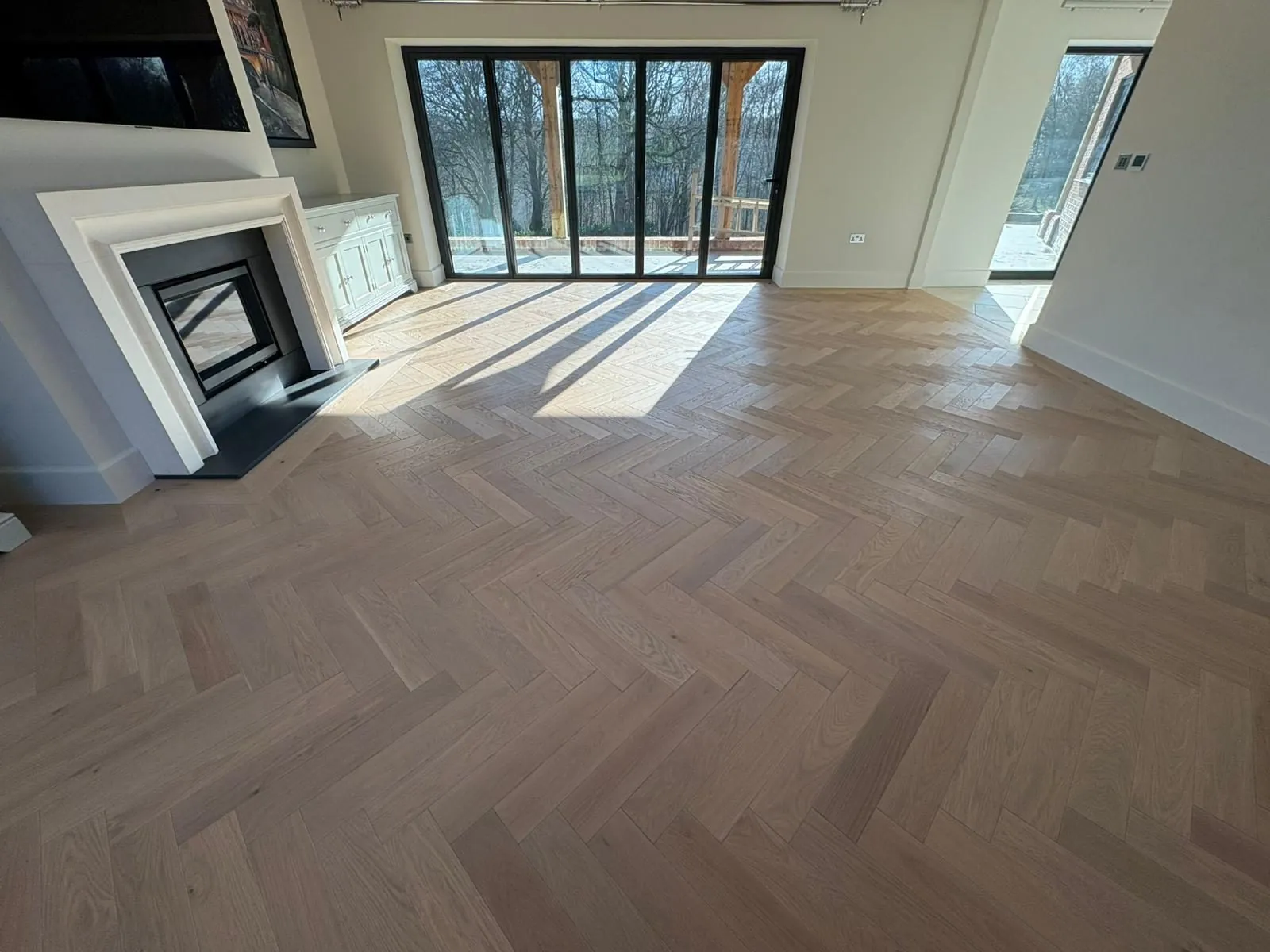 Herringbone oak flooring in a living room with a fireplace and garden doors | Northfold Flooring